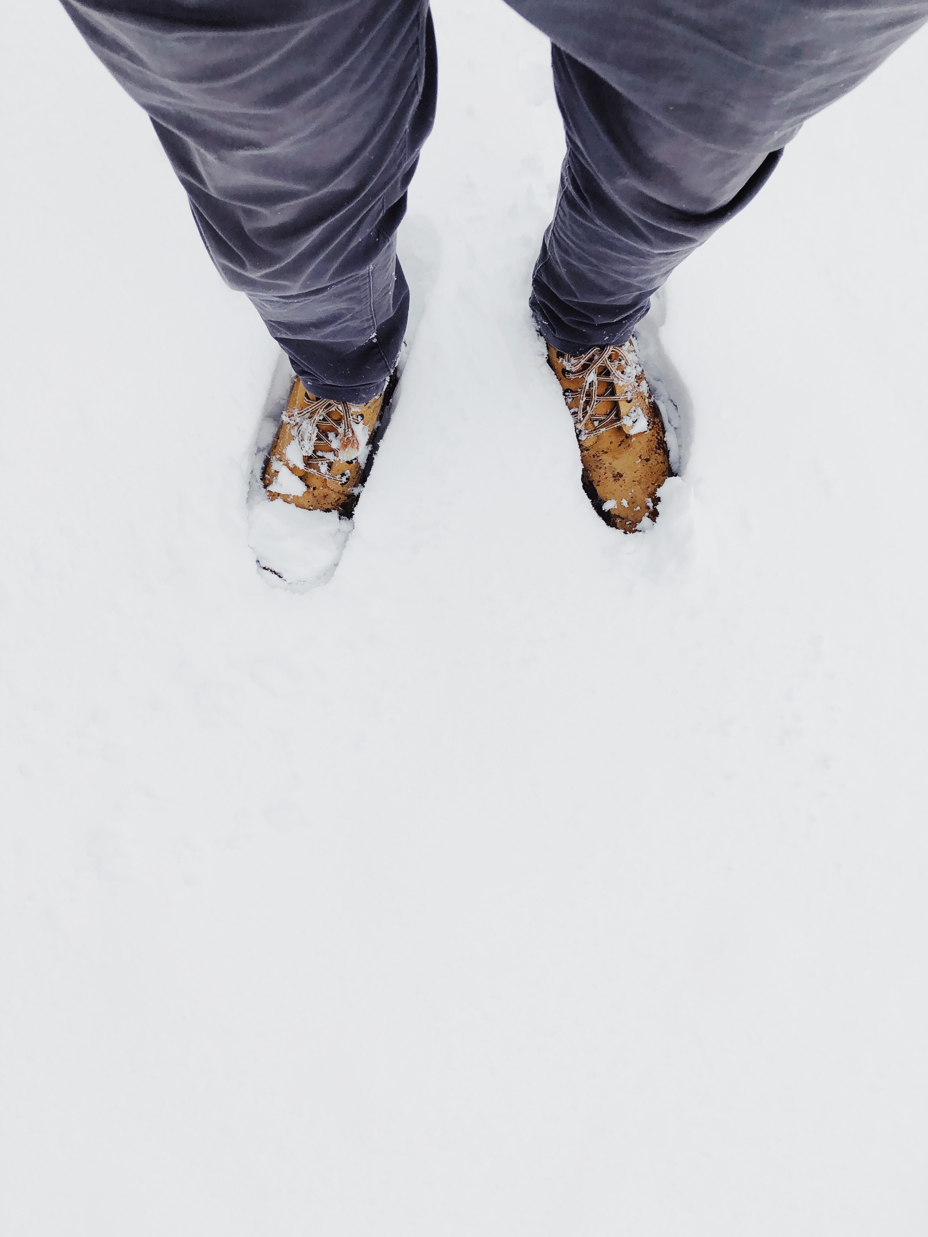 The two feet of a Young adult wearing laced boots in about 3 inches of snow.